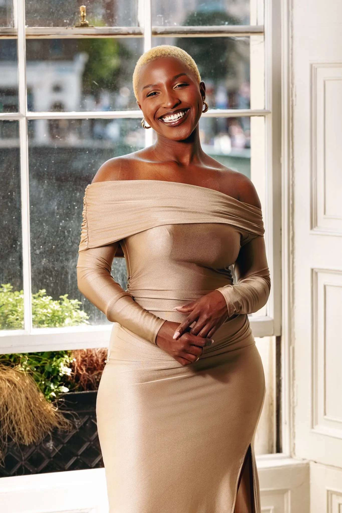 Smiling person in elegant gold dress by a window