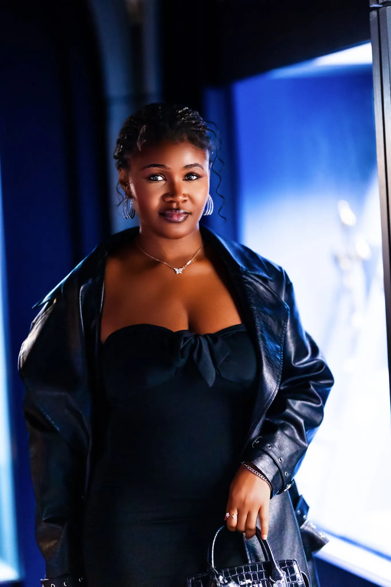 Confident woman in black dress and leather jacket, smiling indoors