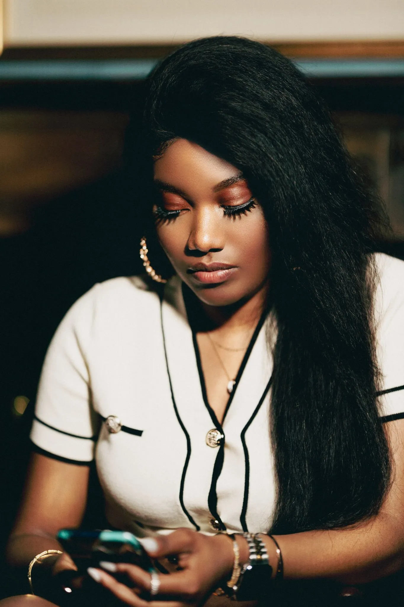 Woman with long hair using a smartphone, wearing a white top.