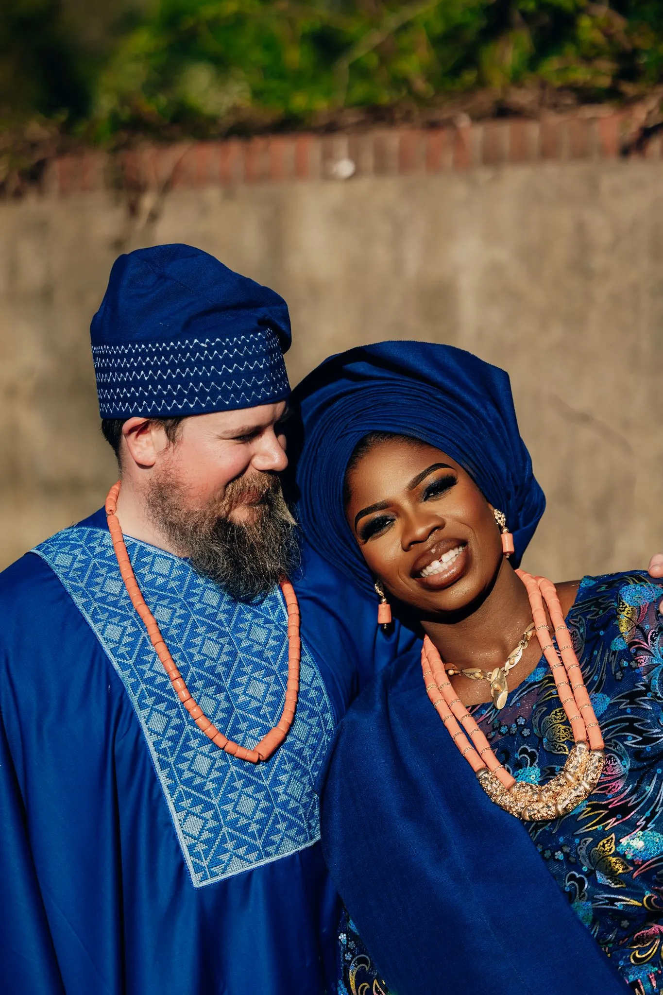 Couple in traditional blue attire with orange beads, smiling outdoors.