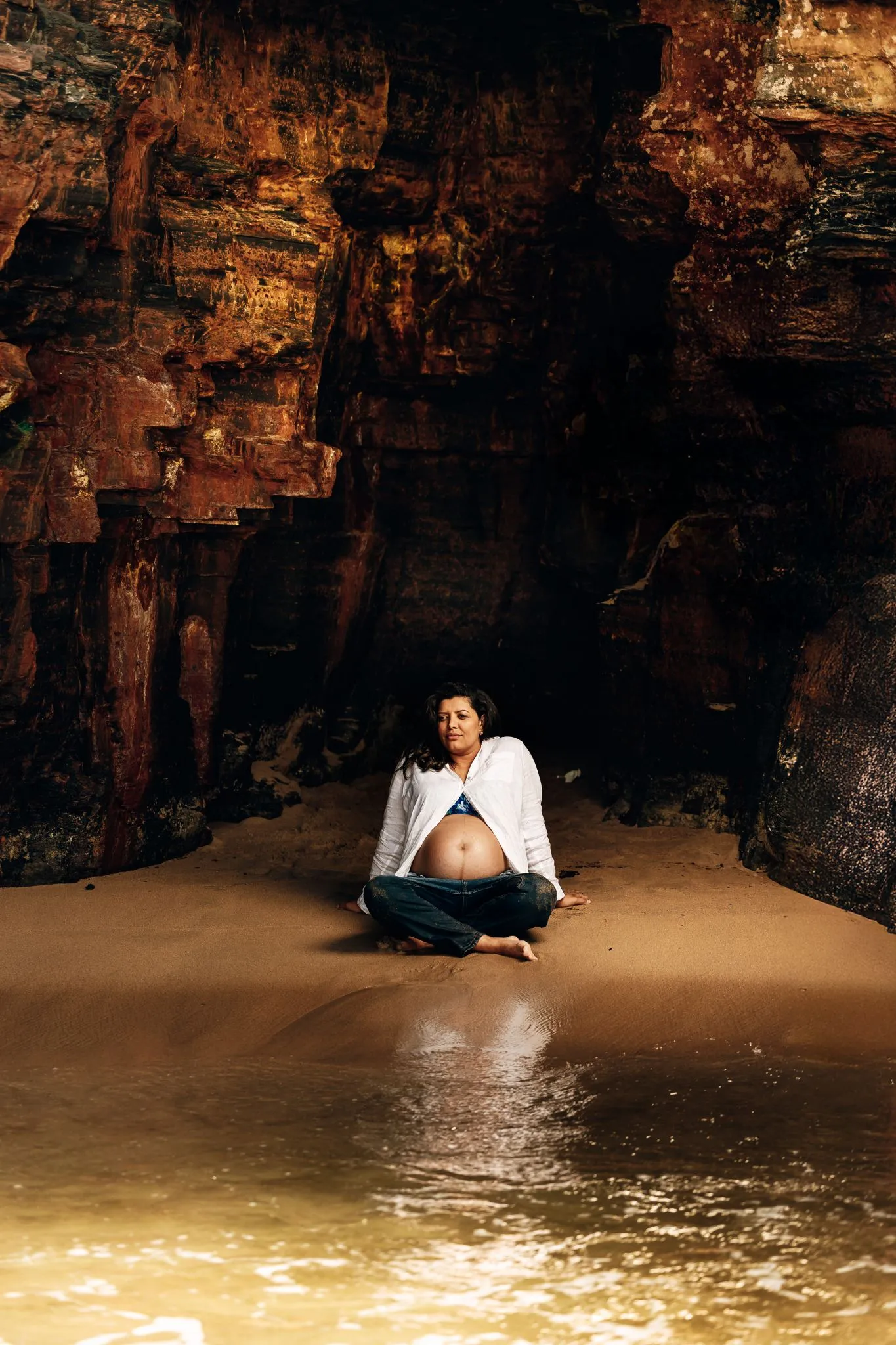 Pregnant woman sitting on a sandy beach near rocky cliffs
