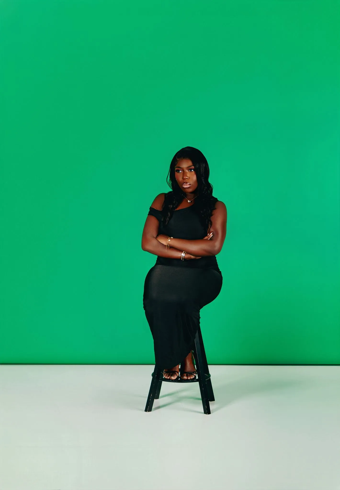 Person in black dress sitting on stool against green background