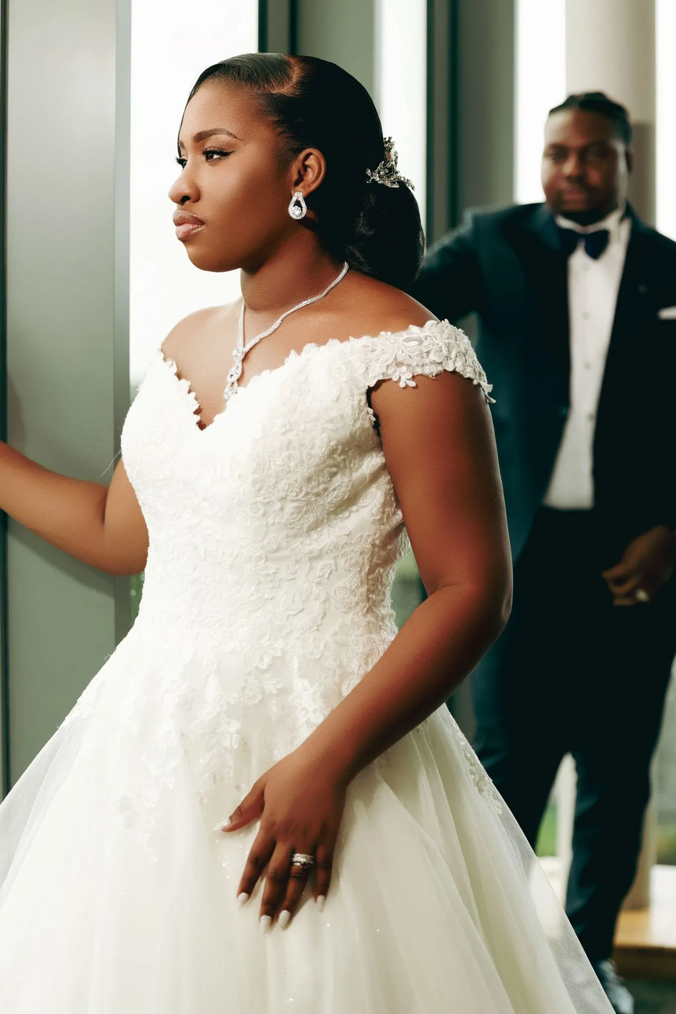 Bride in elegant gown with groom in background at wedding