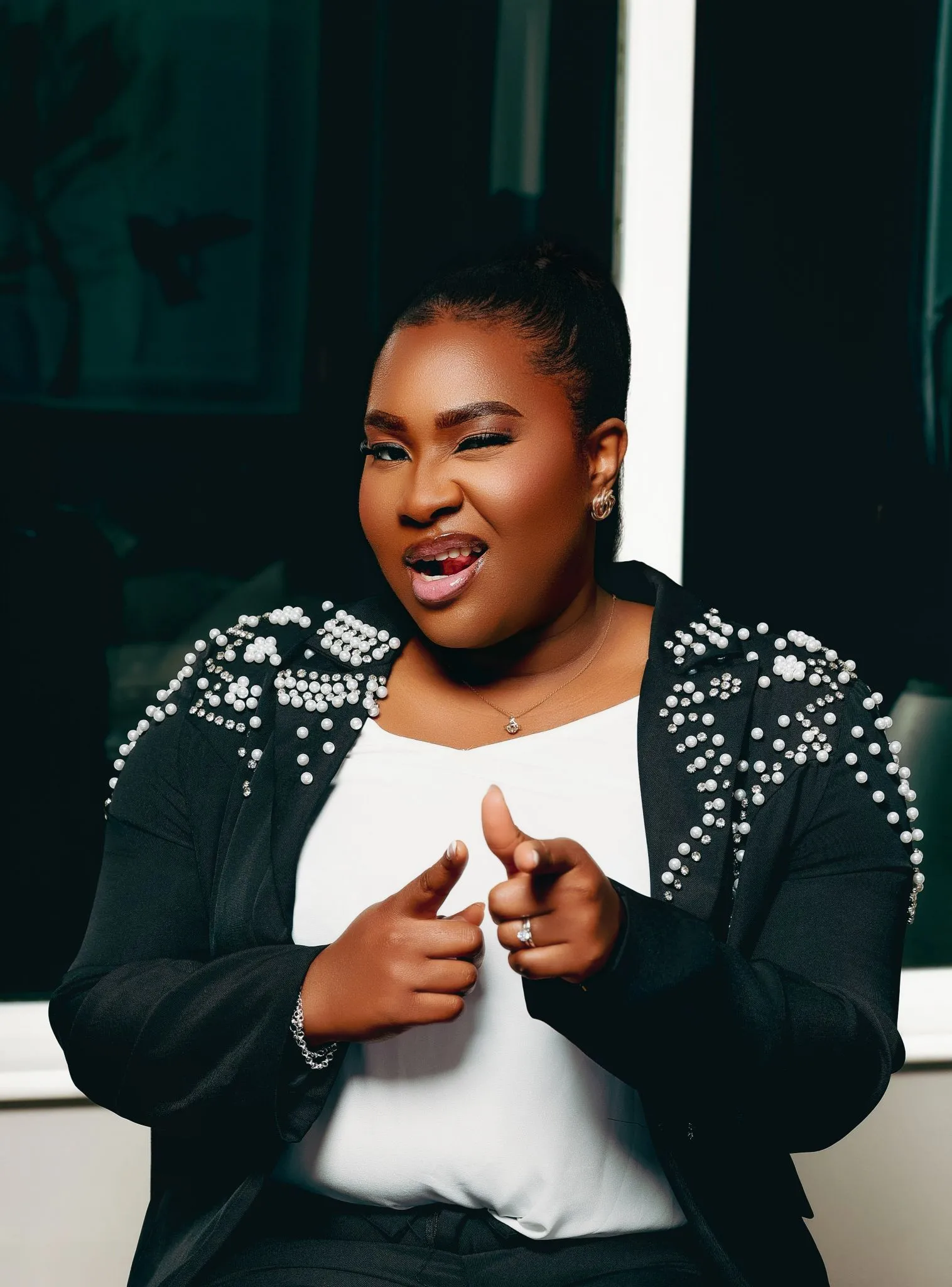 Confident woman smiling and pointing, wearing a pearl-studded jacket.
