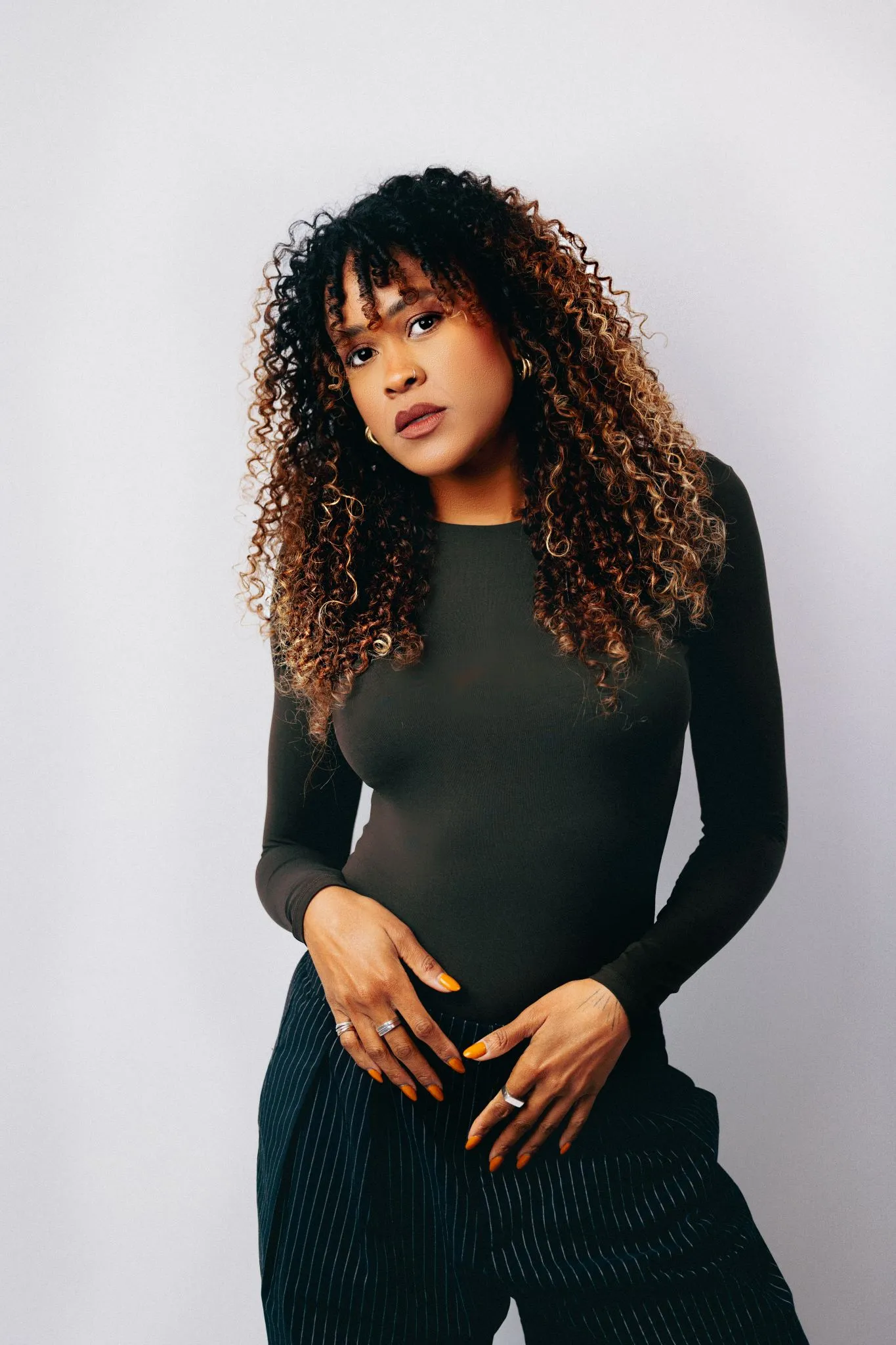 Portrait of a woman with curly hair wearing a black top and striped pants.