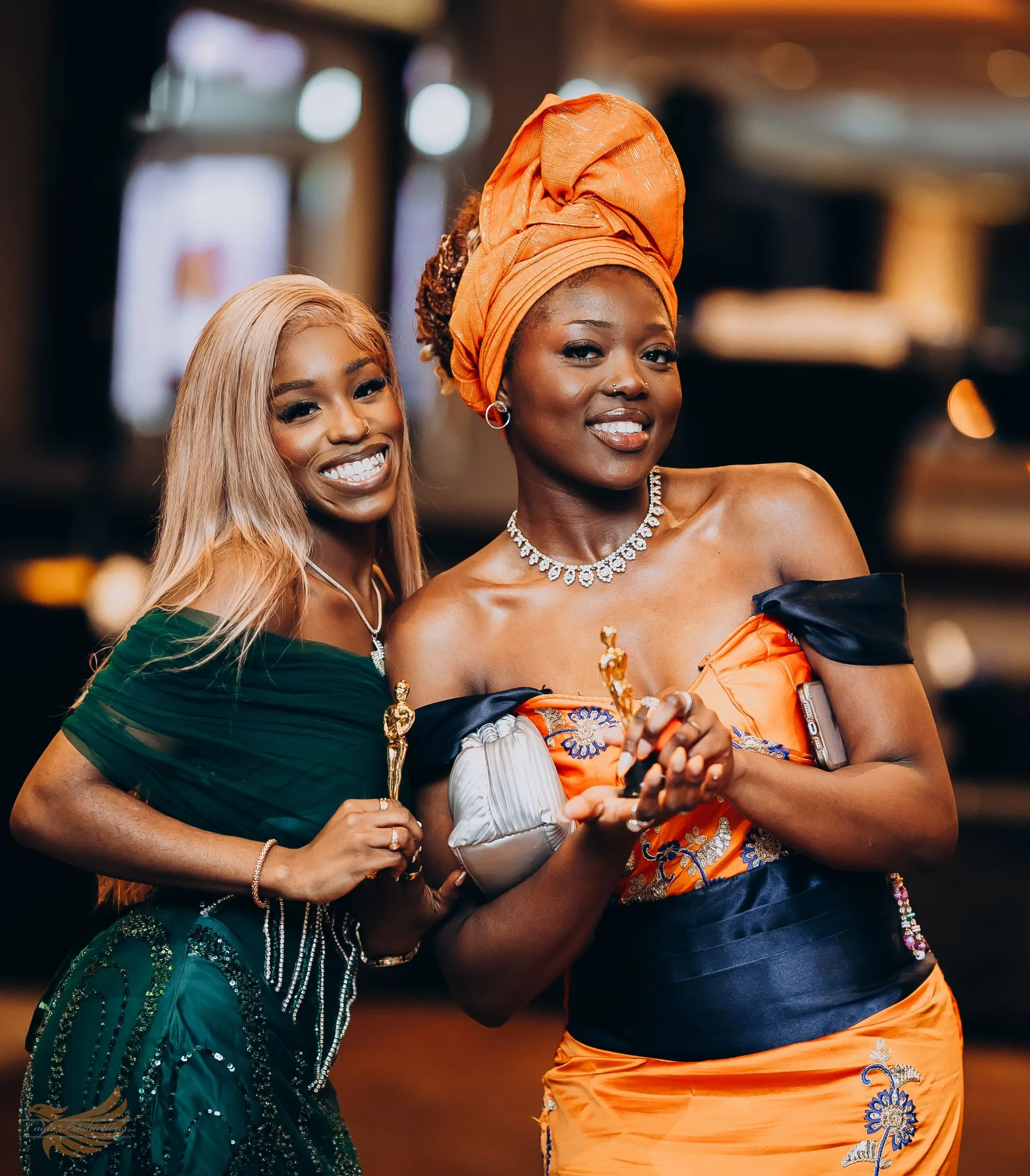 Two women celebrating at an elegant awards event, holding trophies.