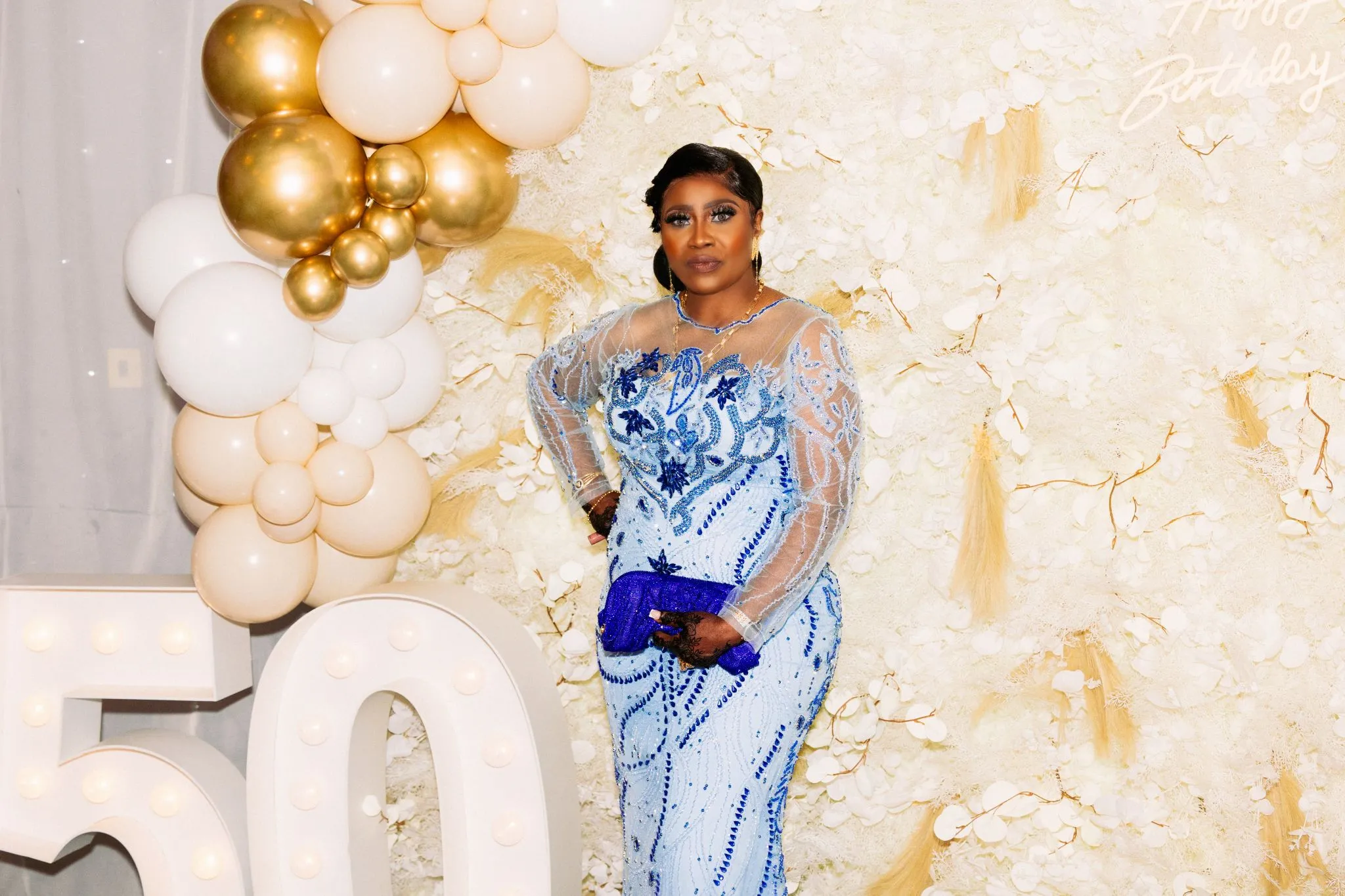 Elegant birthday celebration with woman in blue dress by balloon arch.