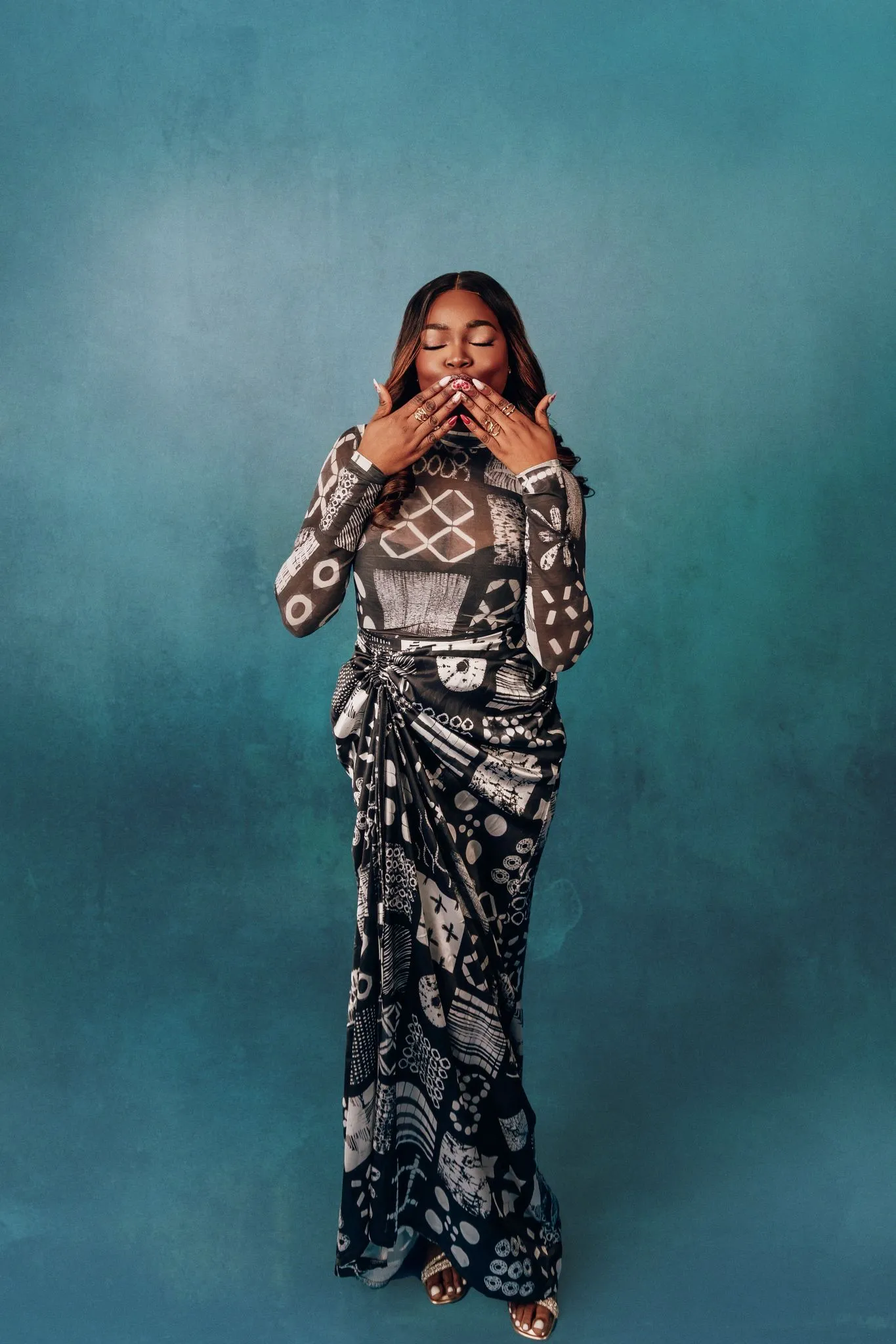 Woman in elegant patterned dress with geometric designs on a blue background.