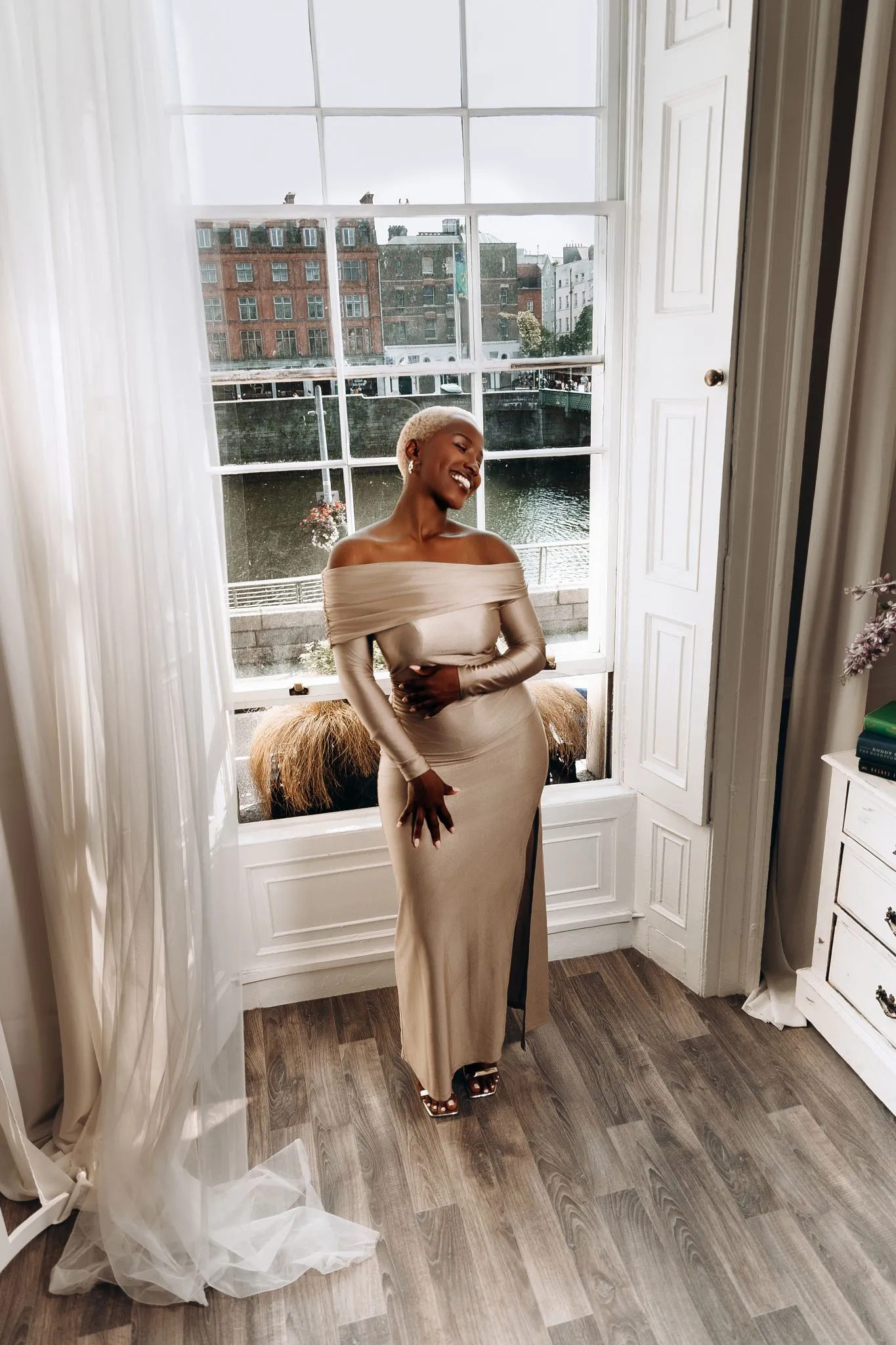 Elegant woman in a stylish dress standing by a large window.