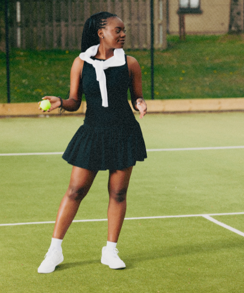 Woman in a black tennis dress holding a tennis ball on an outdoor tennis court
