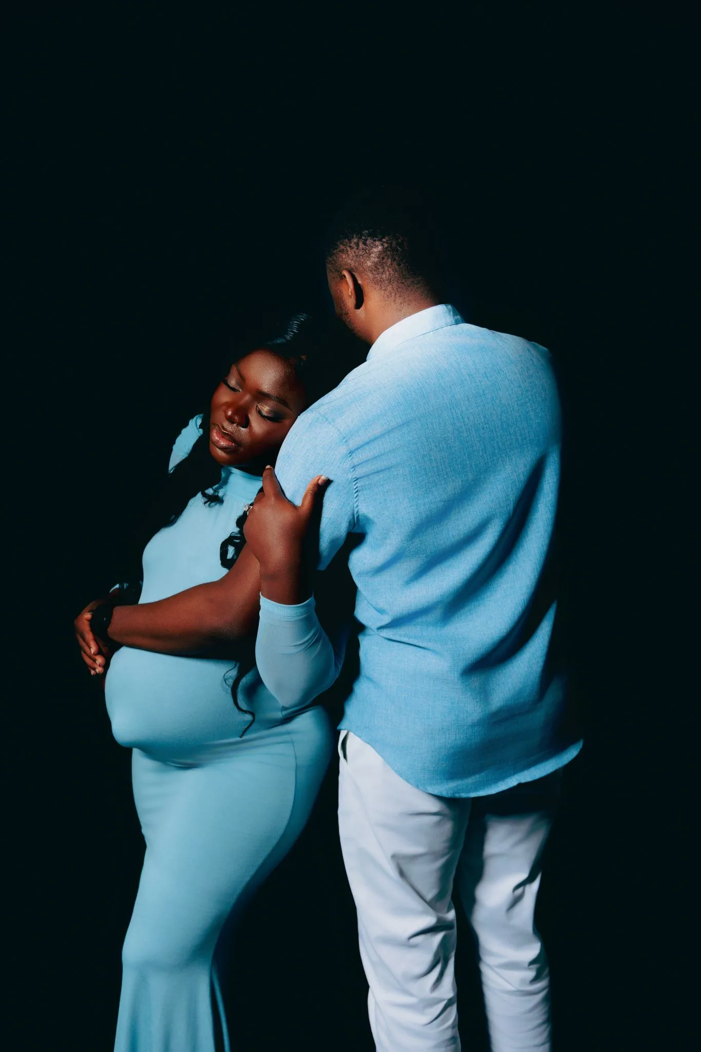 Expecting couple embracing tenderly in matching blue outfits