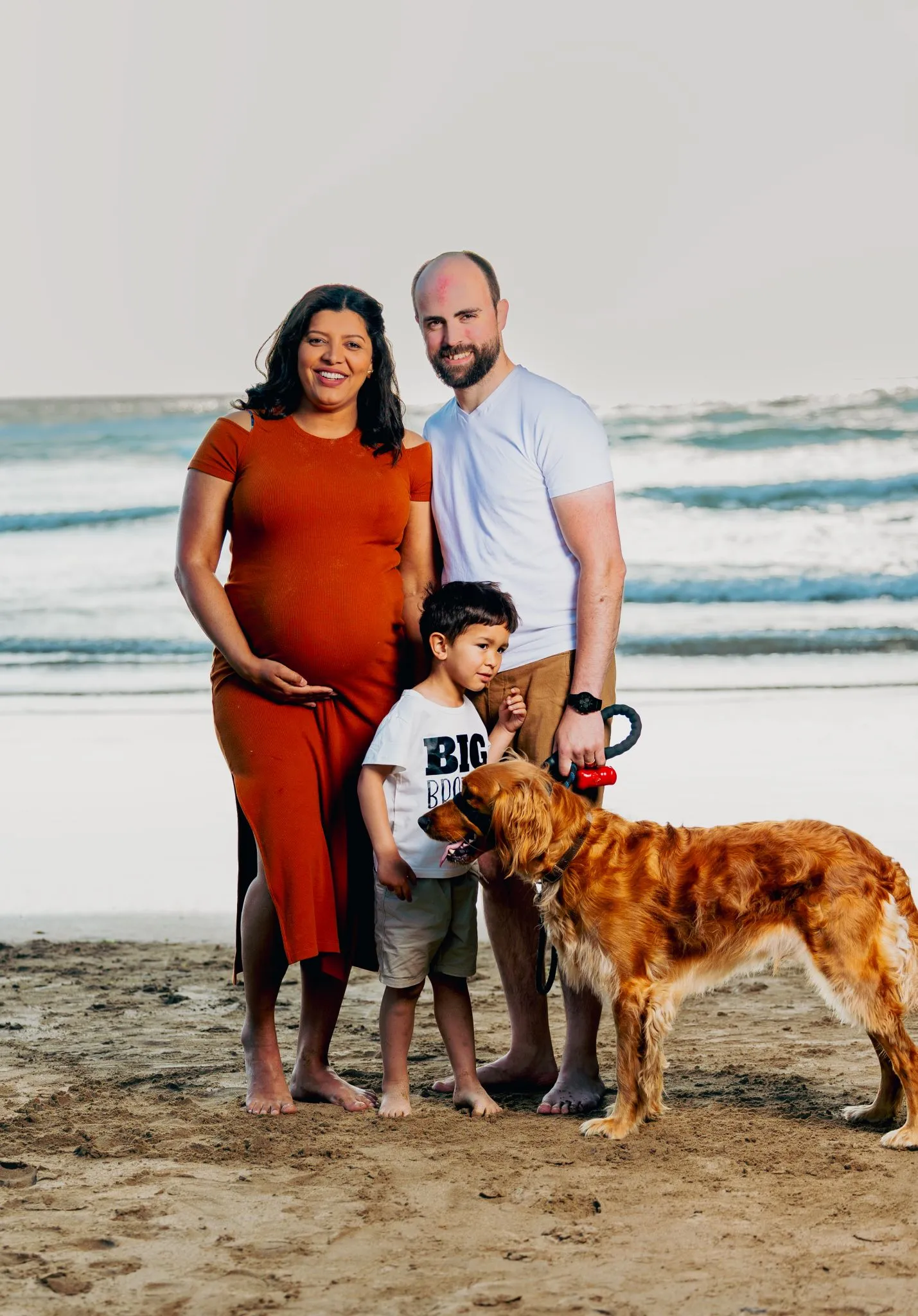 Family at the beach with a dog, expecting a new baby.