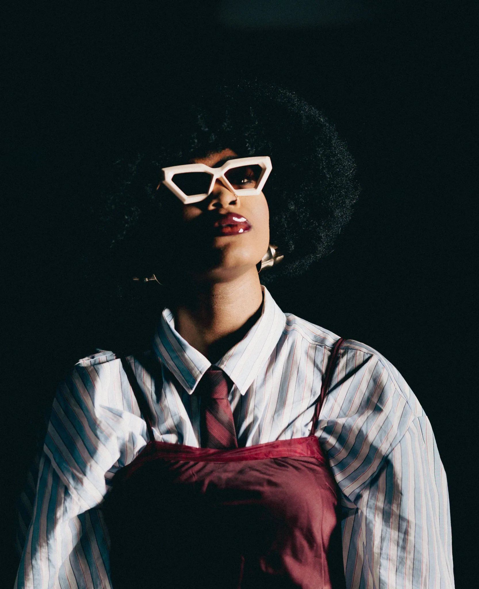 Stylish person with afro hairstyle wearing sunglasses and a striped shirt.