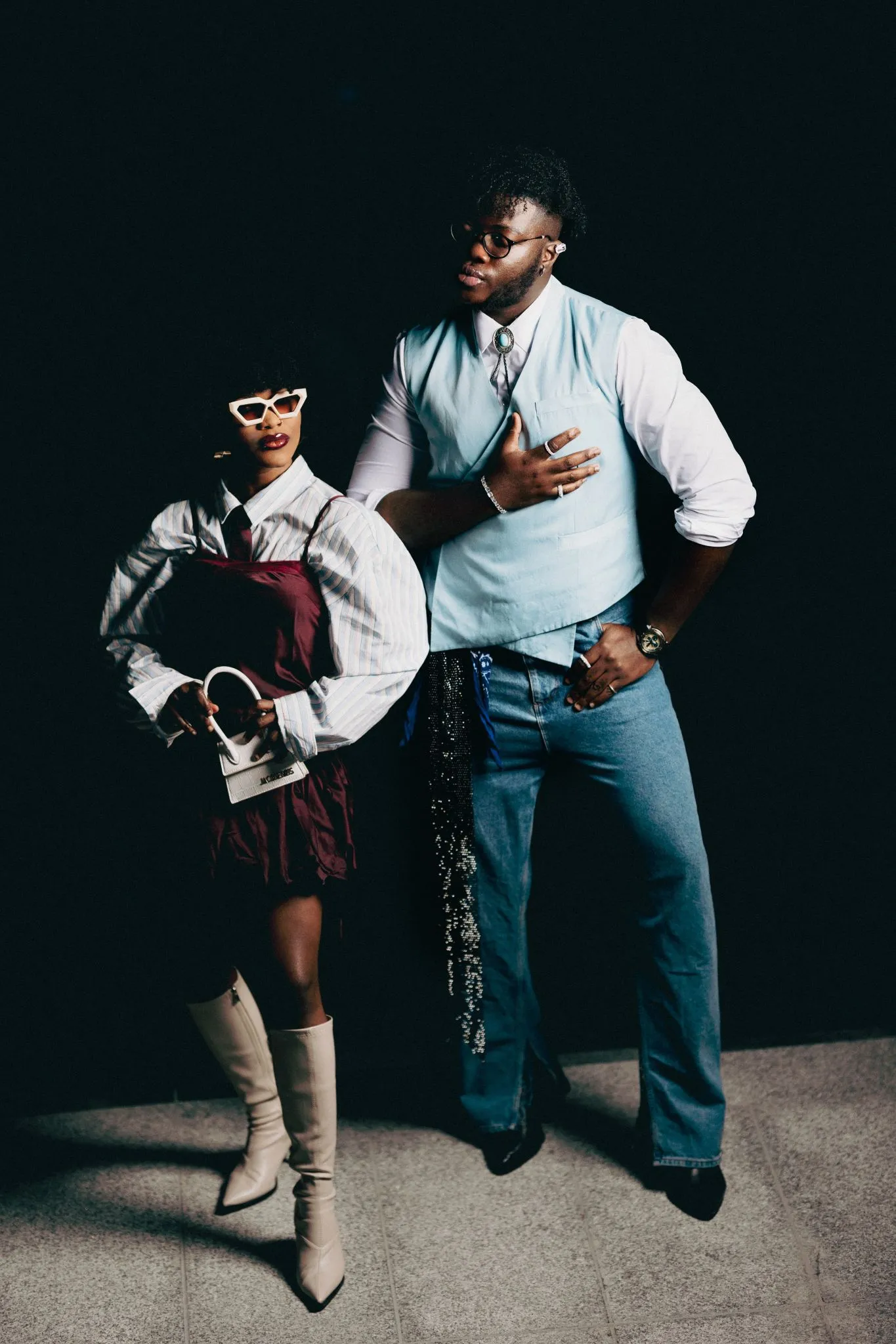Fashionable couple posing in stylish outfits against a dark background.