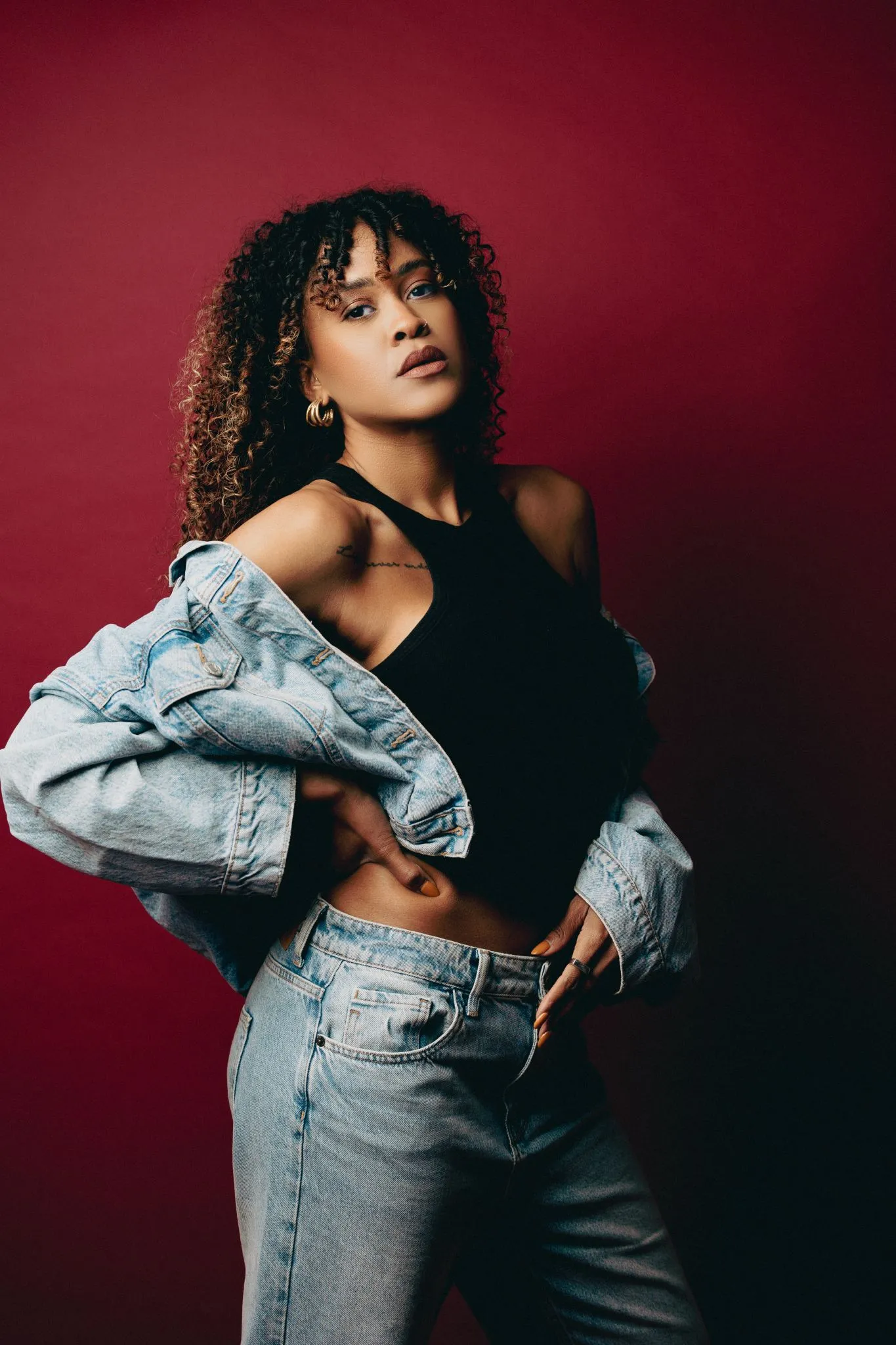 Stylish woman in denim jacket and jeans against red background