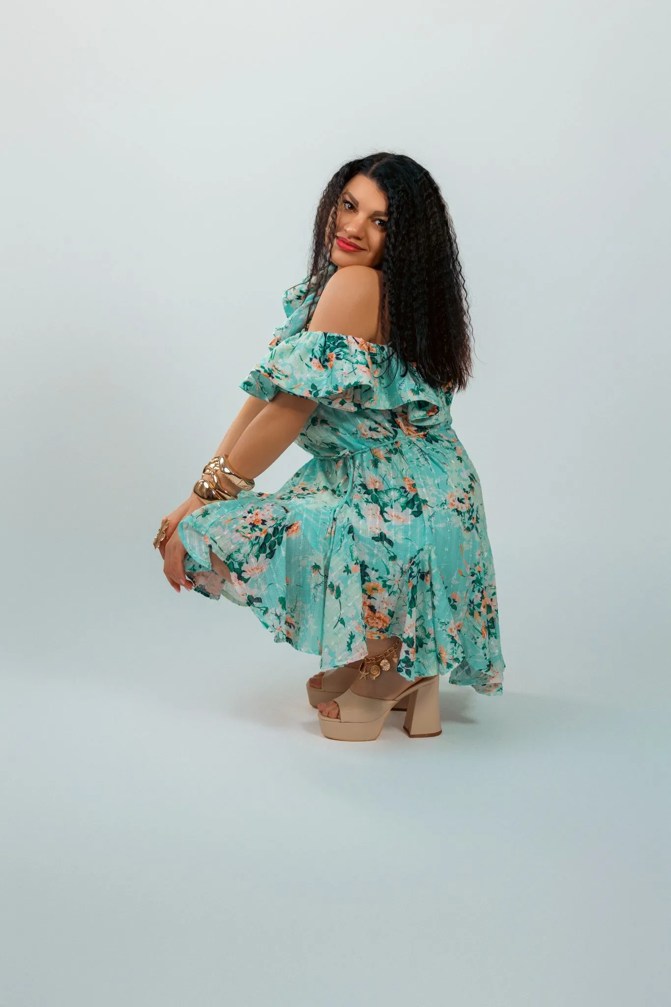 Woman in a floral dress posing confidently against a plain background.