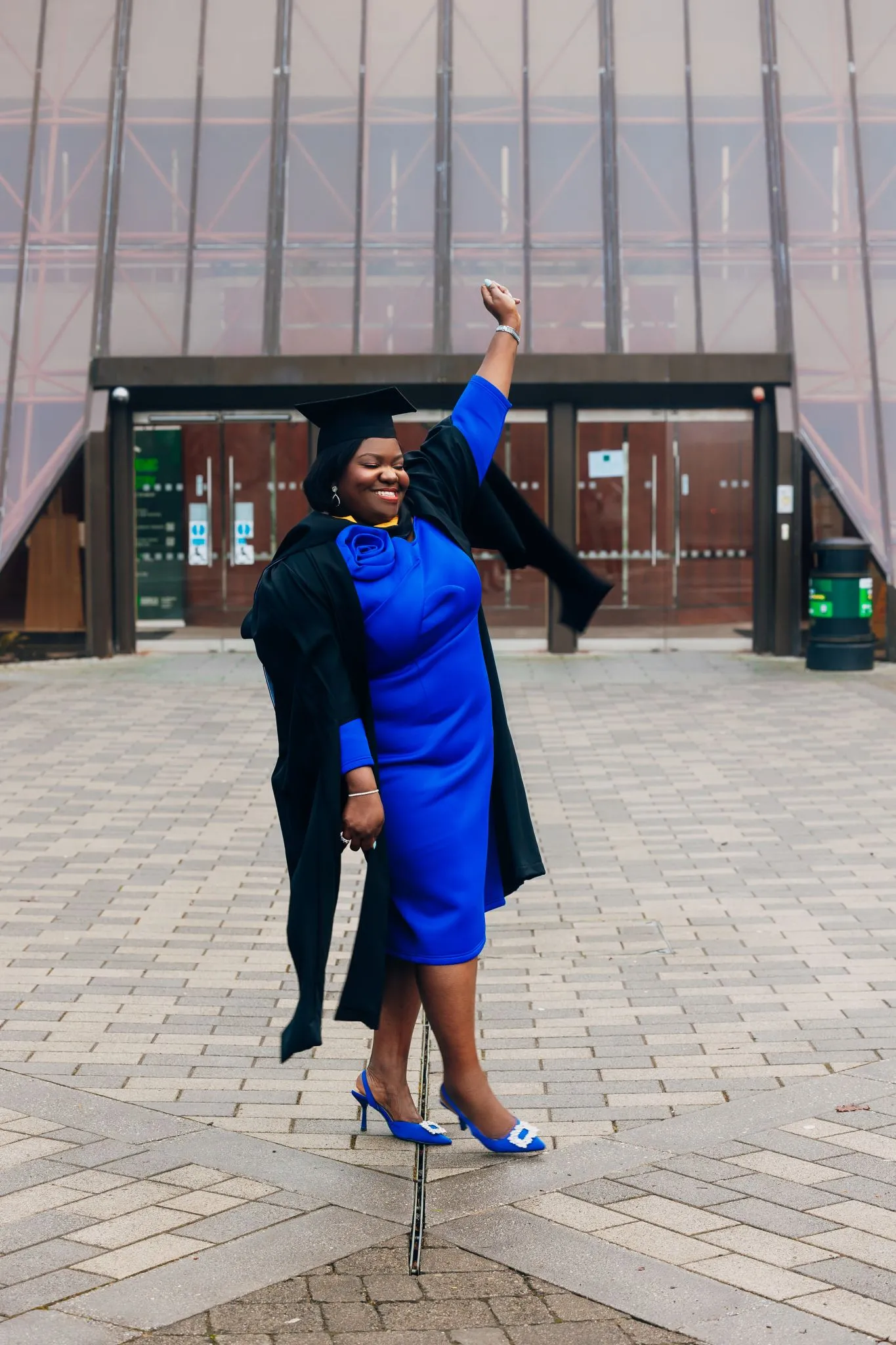 Graduate celebrating outdoors in a blue dress and cap and gown.