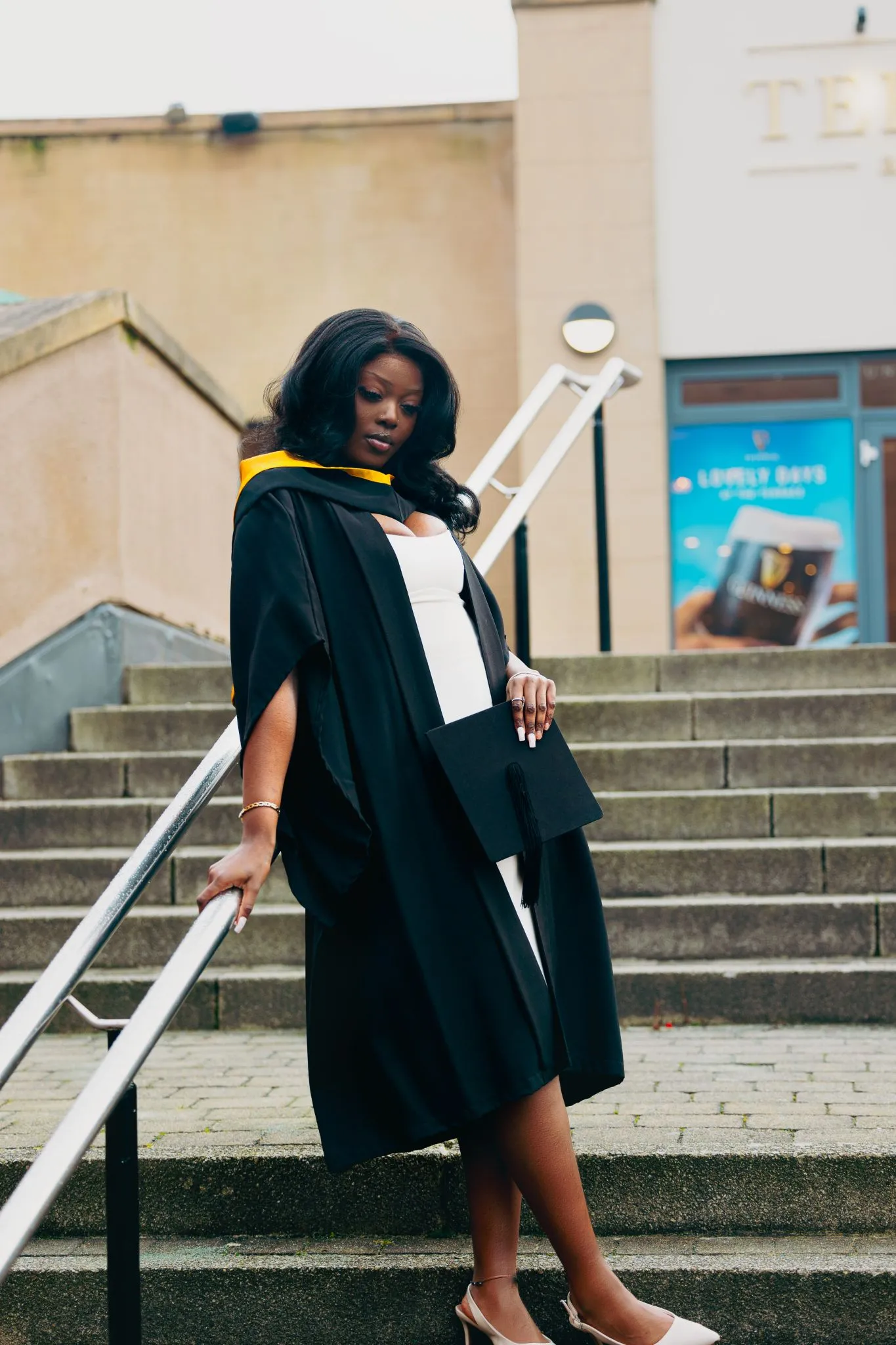 Graduate in cap and gown standing on outdoor steps