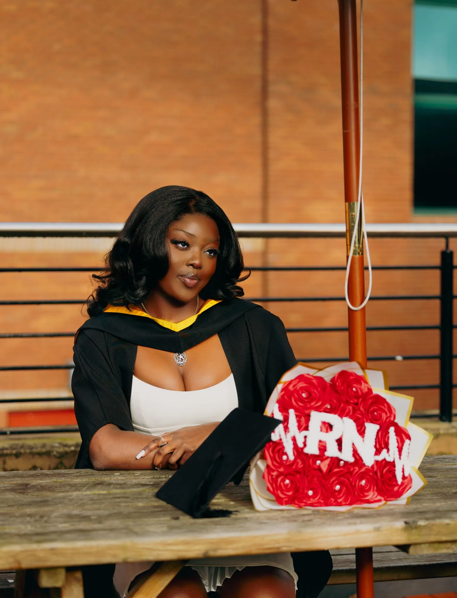 Graduate celebrating outdoors with cap and flowers on a sunny day.
