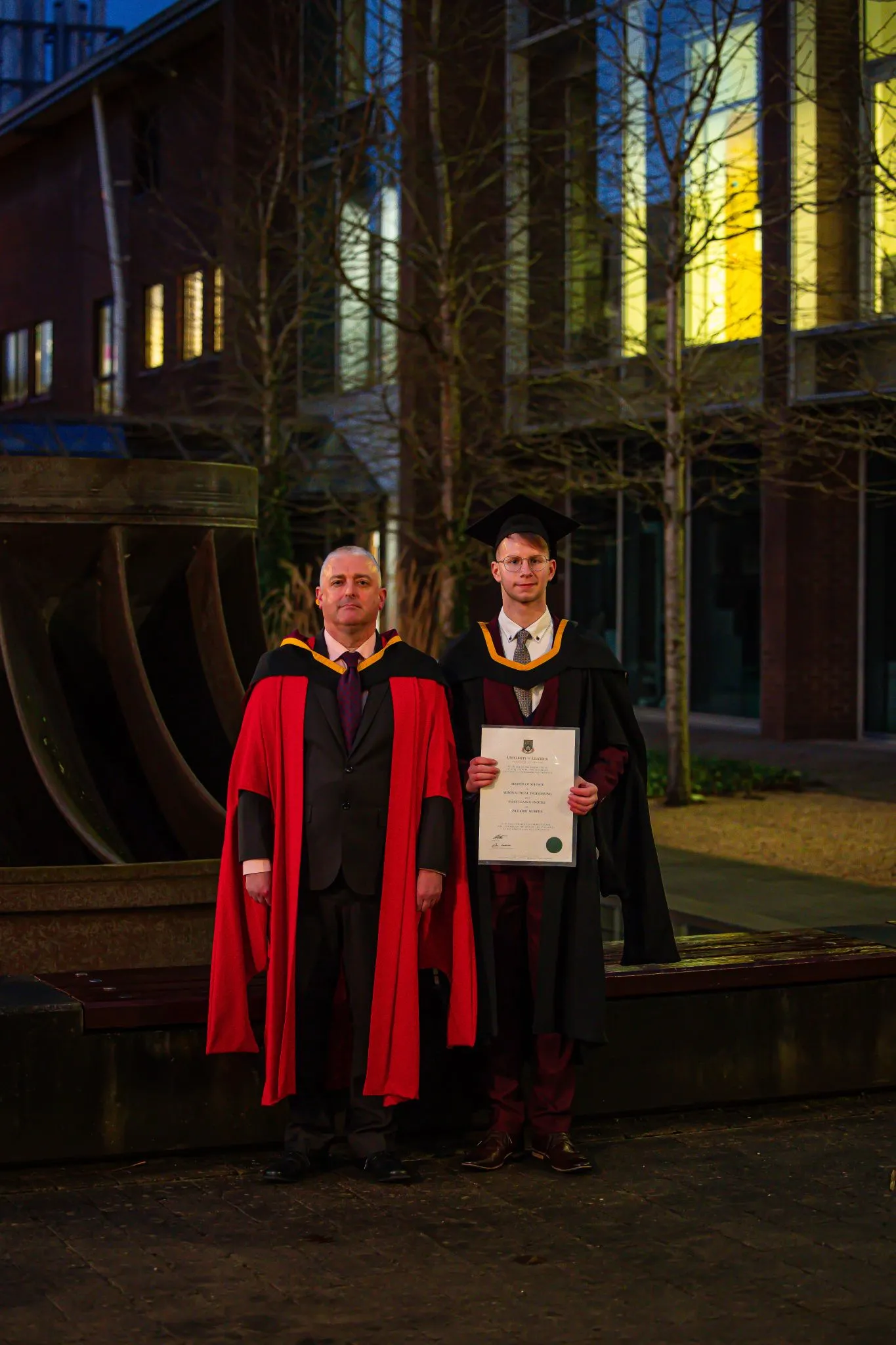 Graduates in caps and gowns at night ceremony, holding diploma.