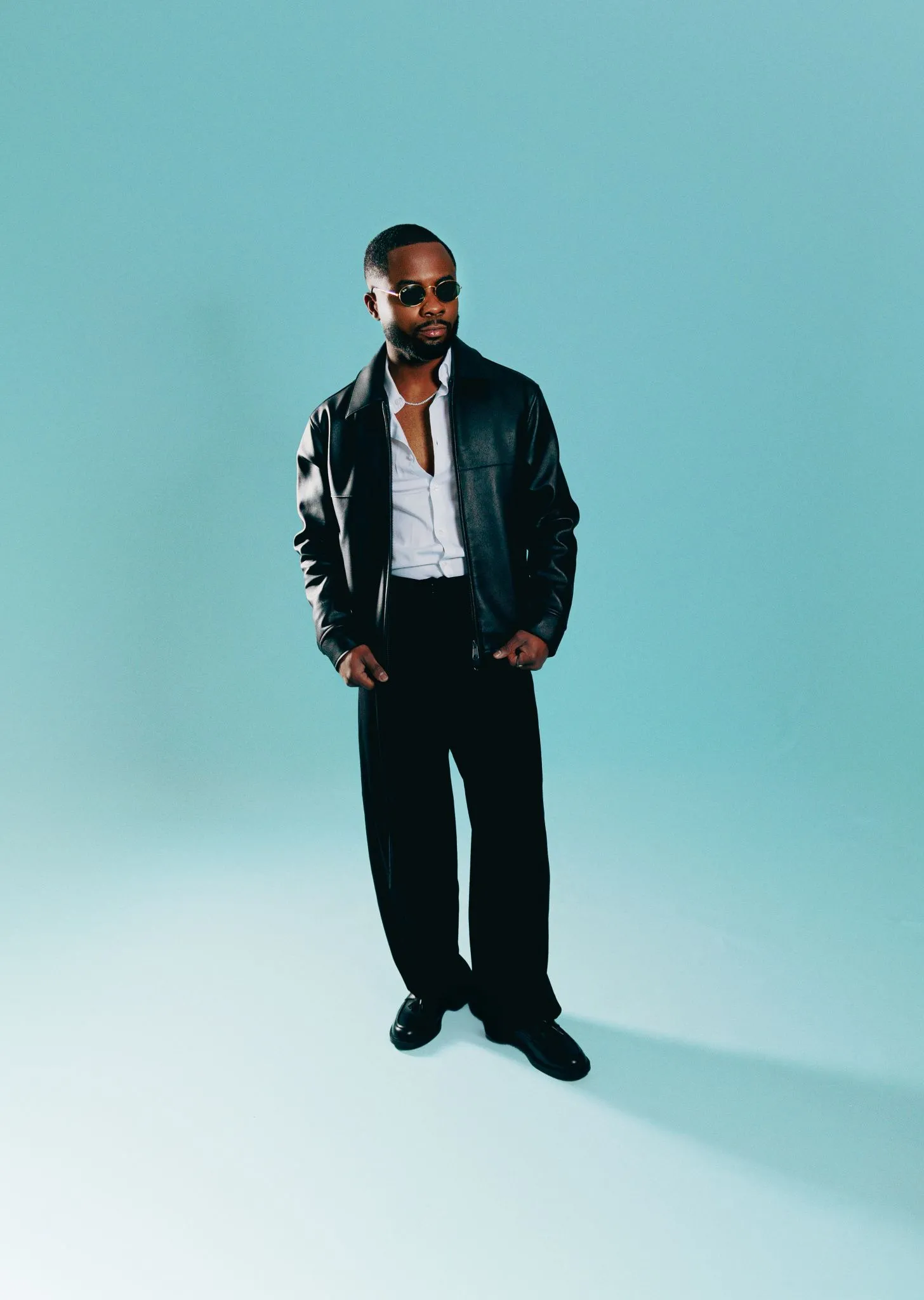 Man in a leather jacket standing confidently against a blue background.