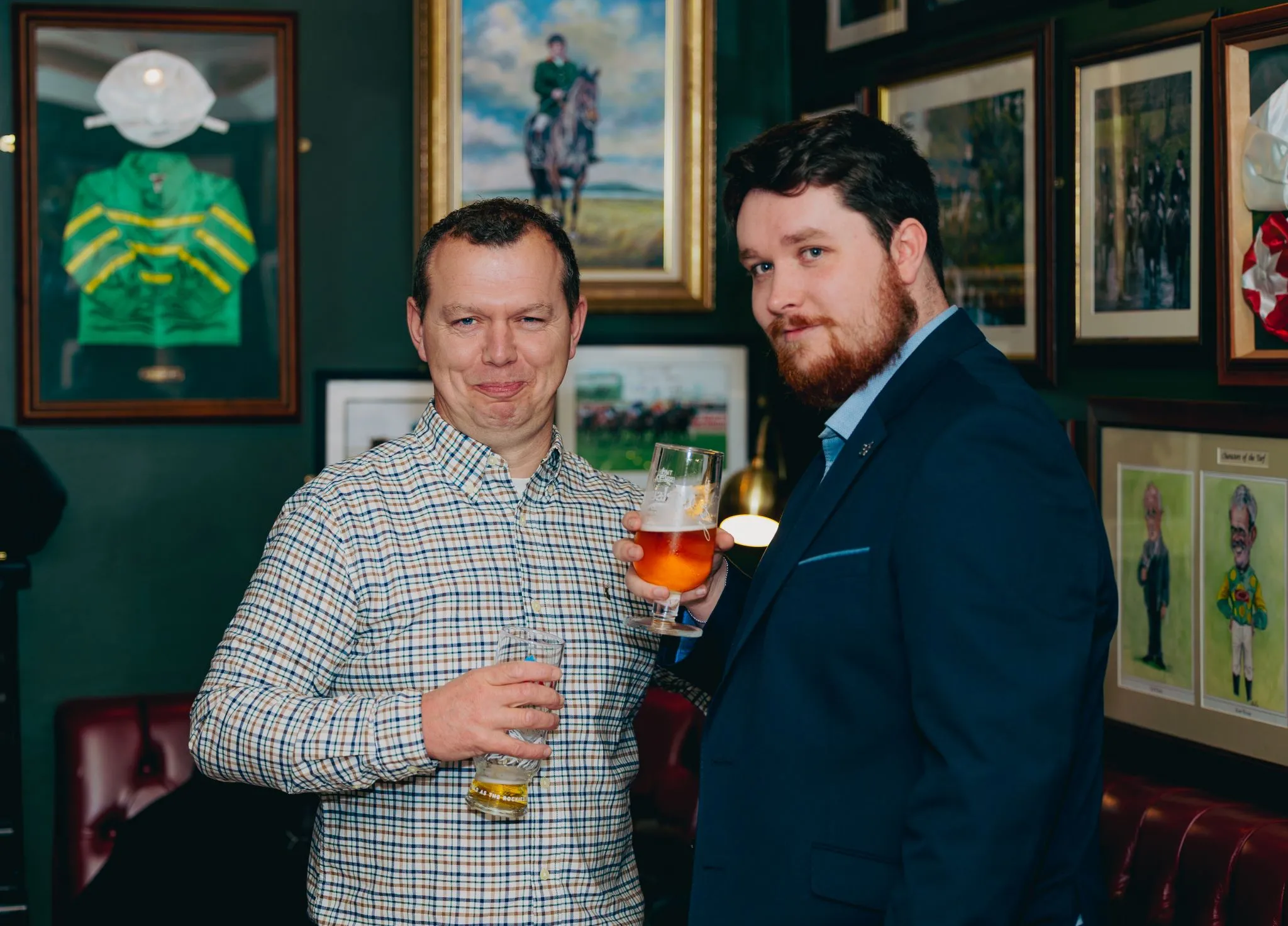 Two men enjoying drinks at a pub with framed art on the walls.
