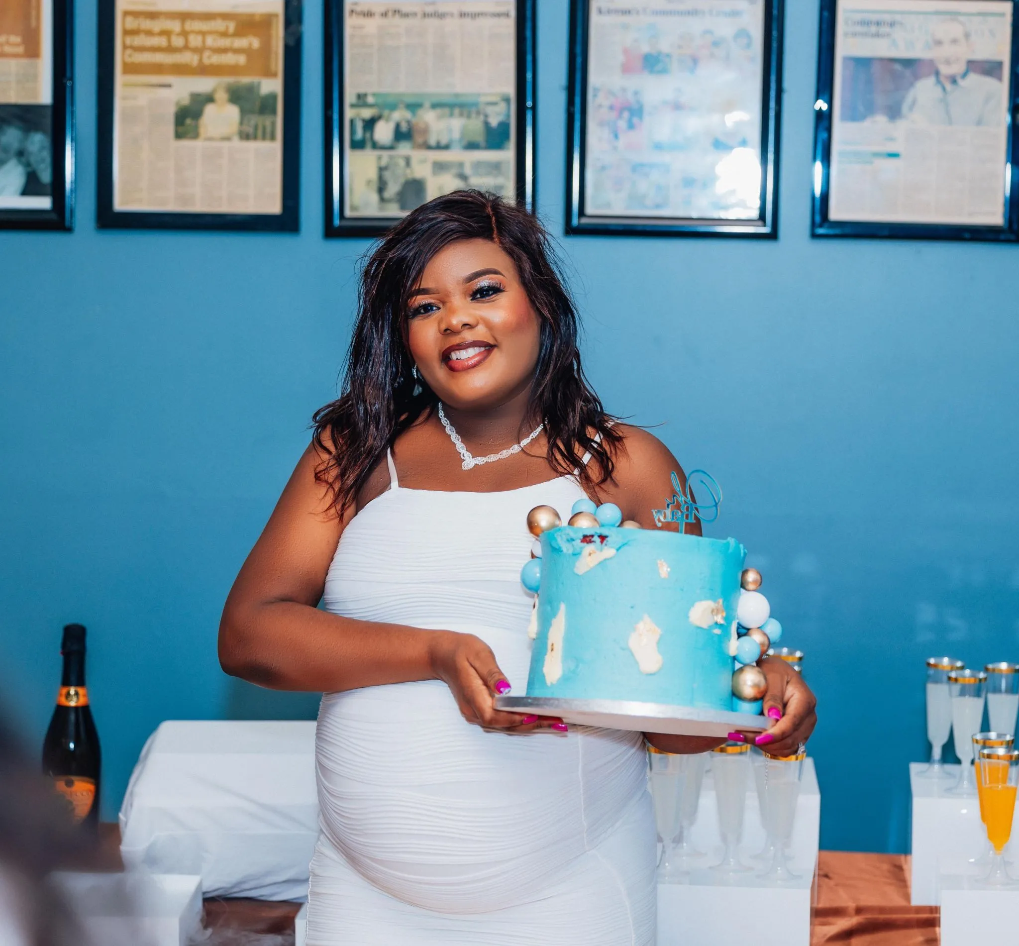Pregnant woman holding a blue celebration cake at a party.