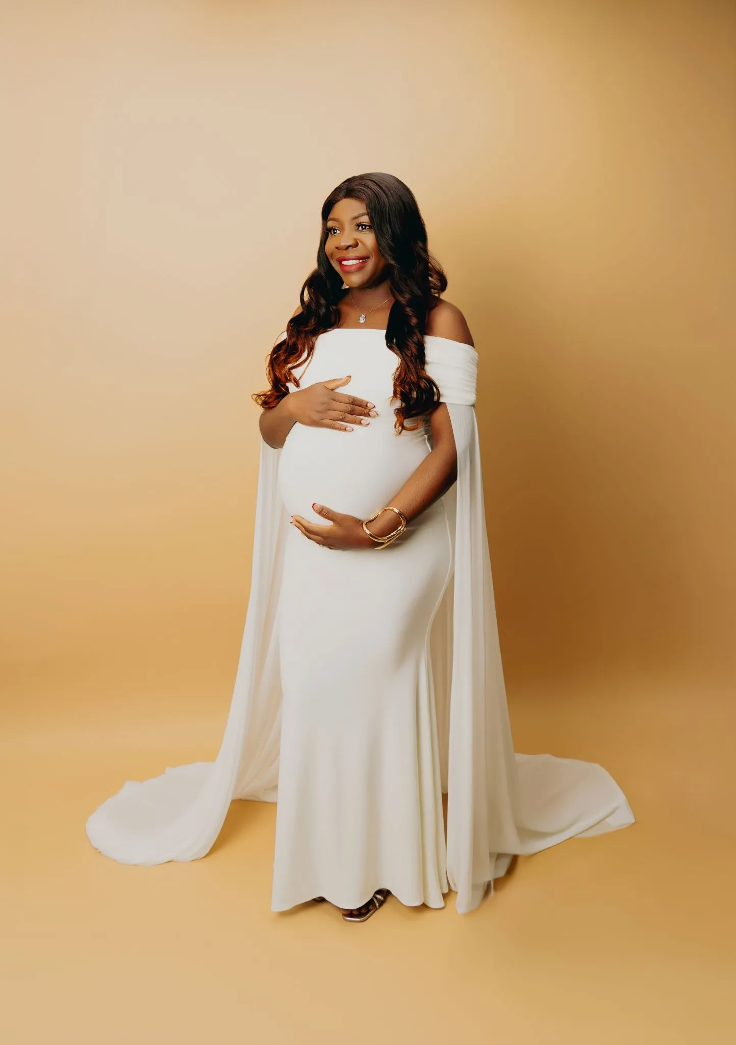 Elegant pregnancy photoshoot with woman in white gown on beige background