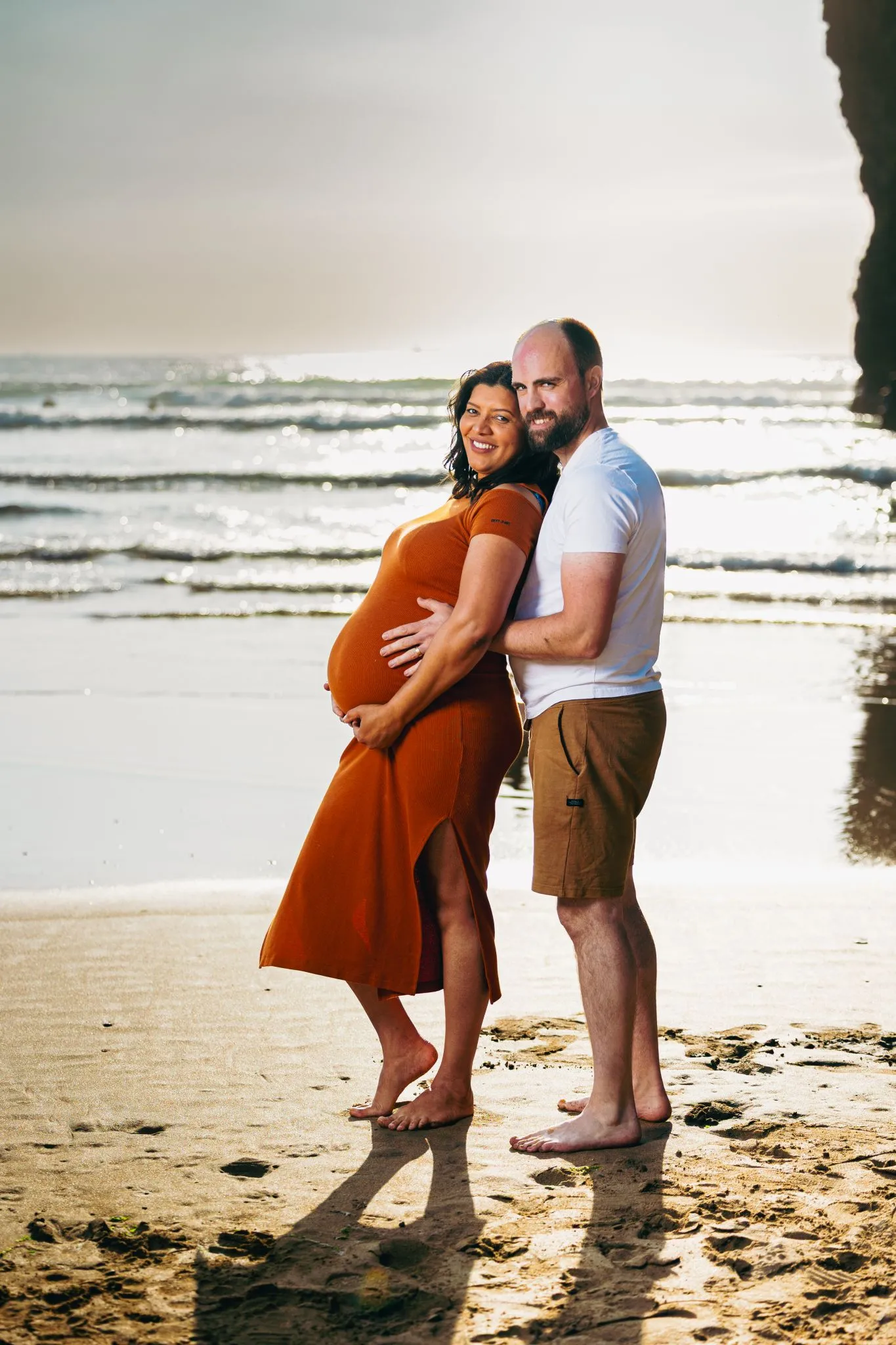 Pregnant couple embracing on a sunny beach.