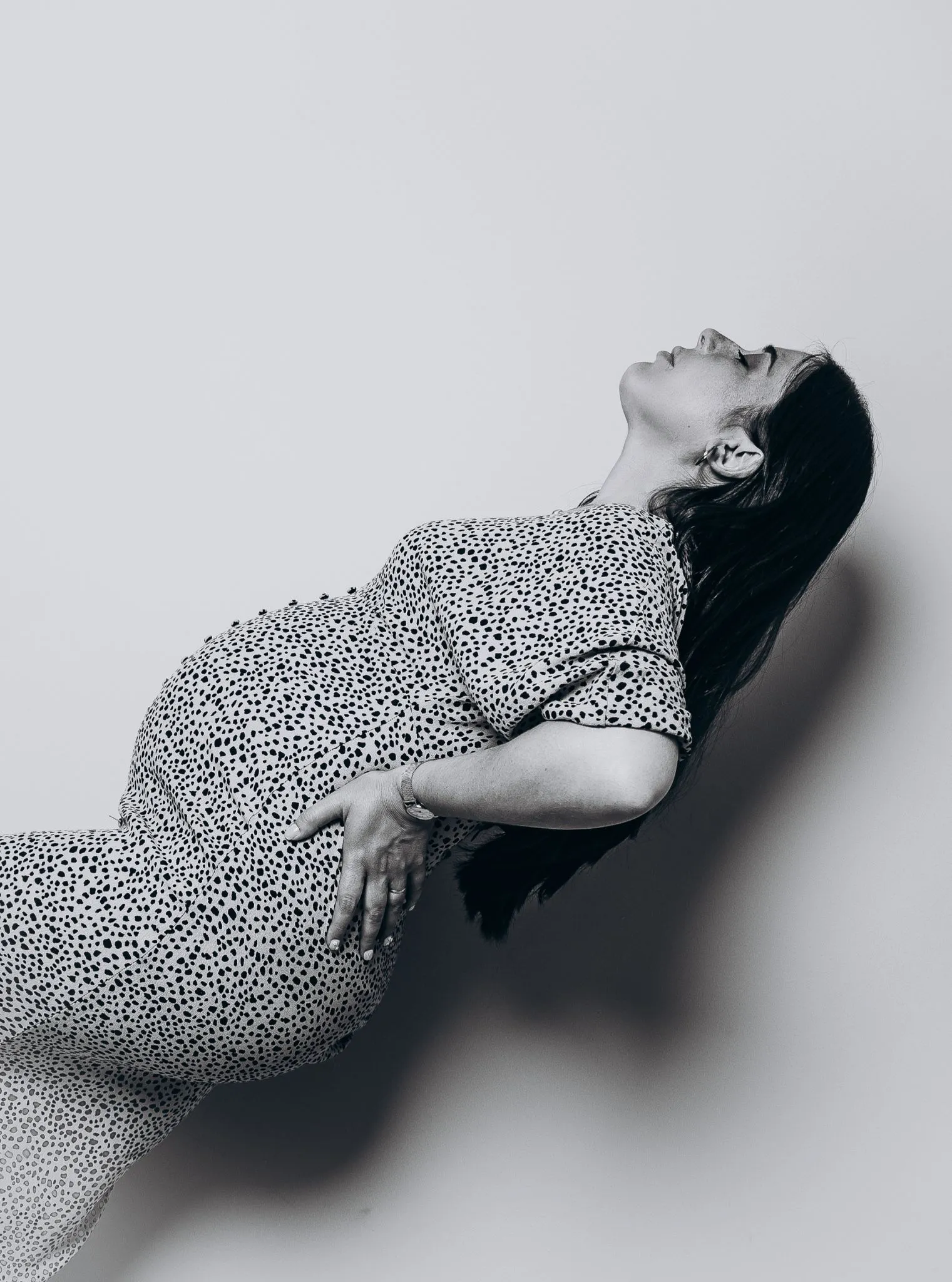 Profile of a pregnant woman in a dotted dress leaning back gracefully.