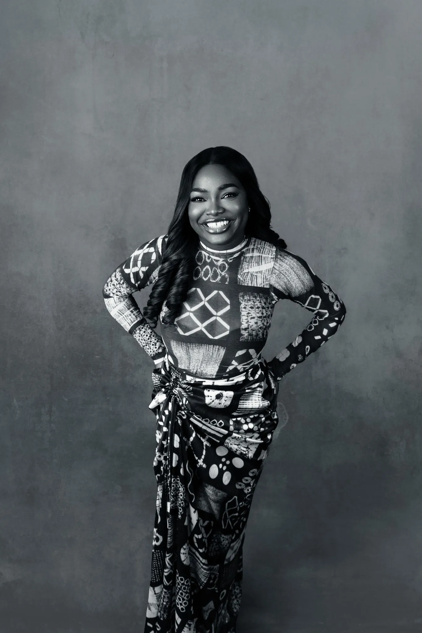 Smiling woman in patterned dress standing confidently.