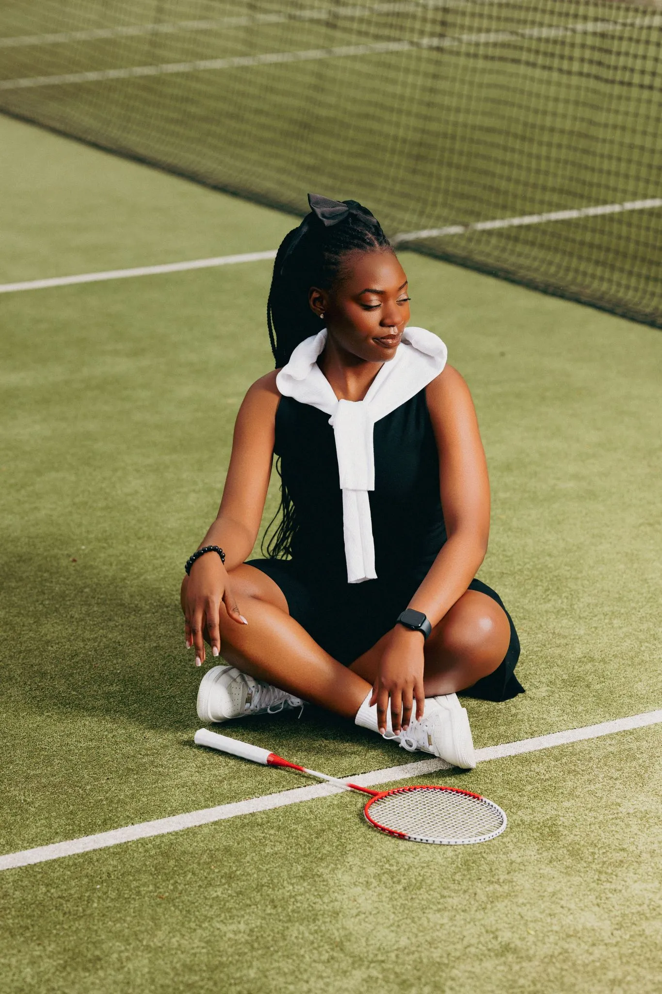 Tennis player sitting on court with racket, wearing black and white outfit.