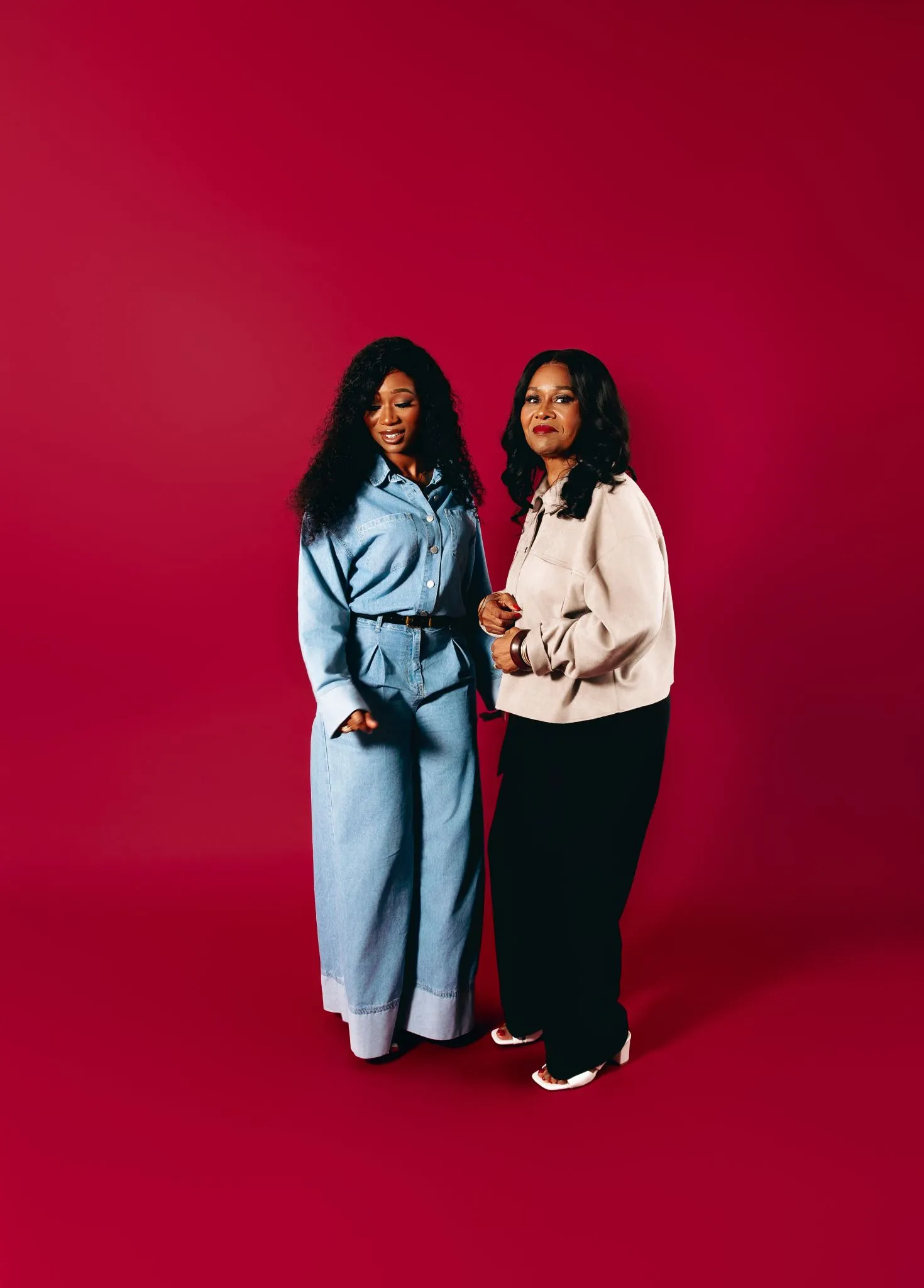 Two women in stylish outfits against a red background