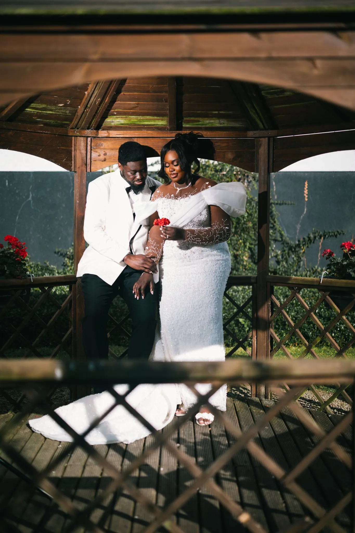 Wedding couple in elegant attire under a wooden gazebo.