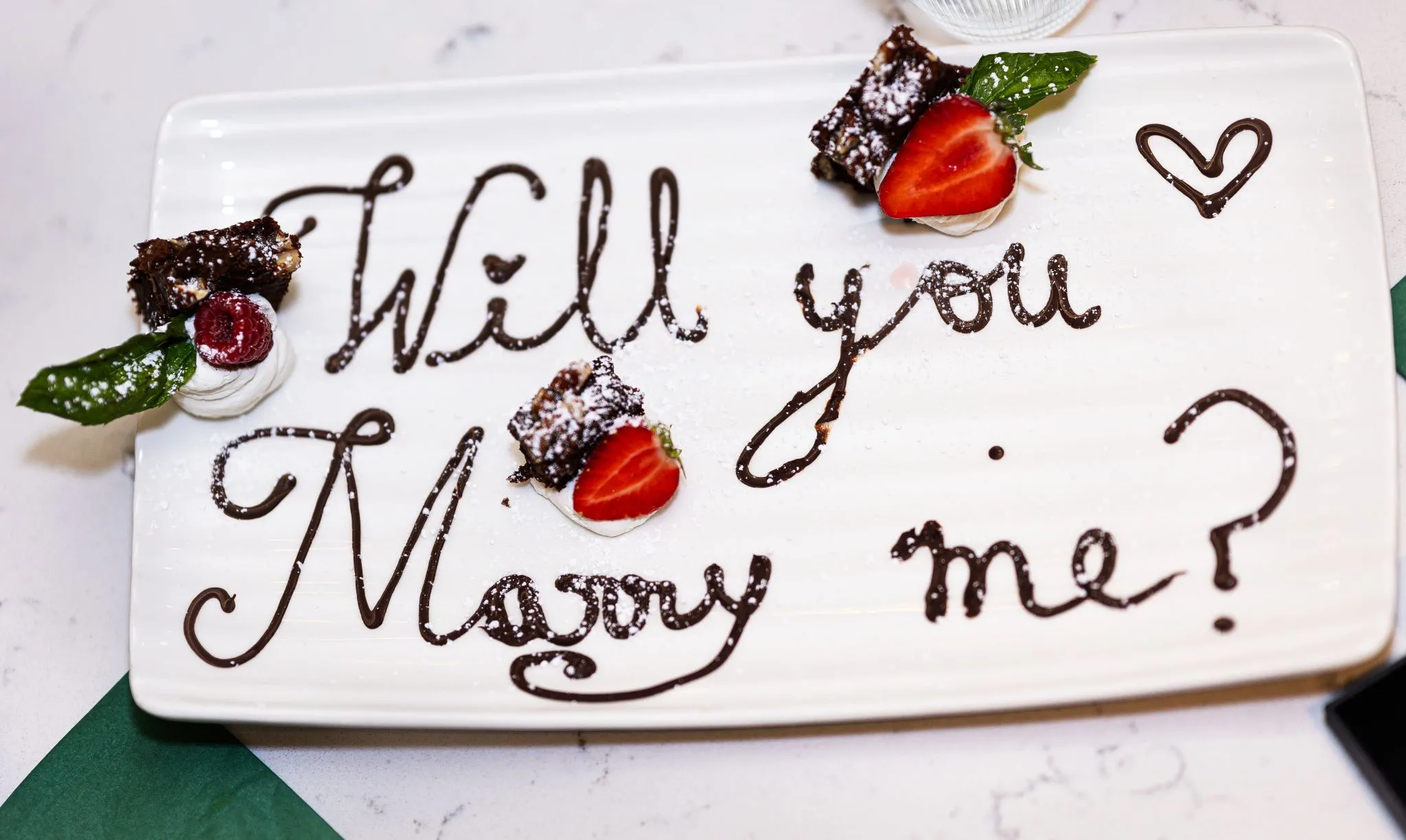 Chocolate message on a plate asking 'Will you marry me?' with strawberries.