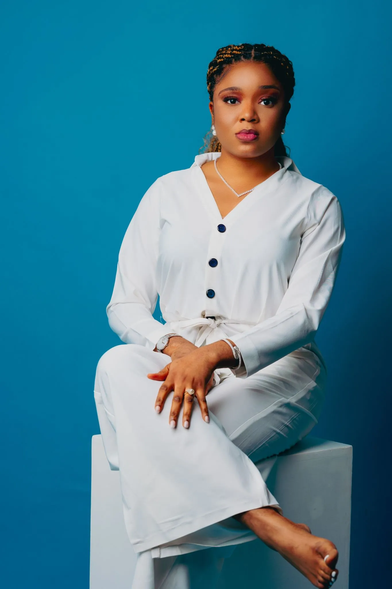 Woman in white outfit sitting gracefully against blue background